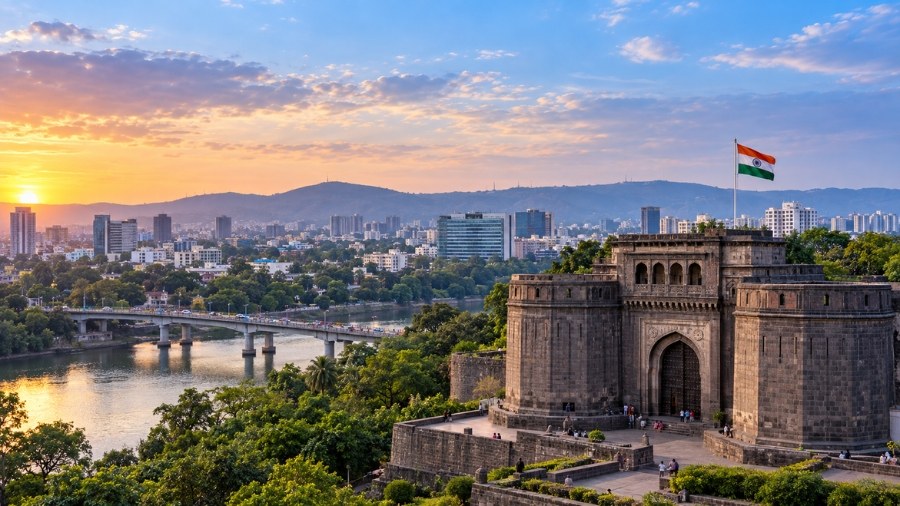 Historic stone gateway with an Indian flag in front of the Pune skyline at sunset